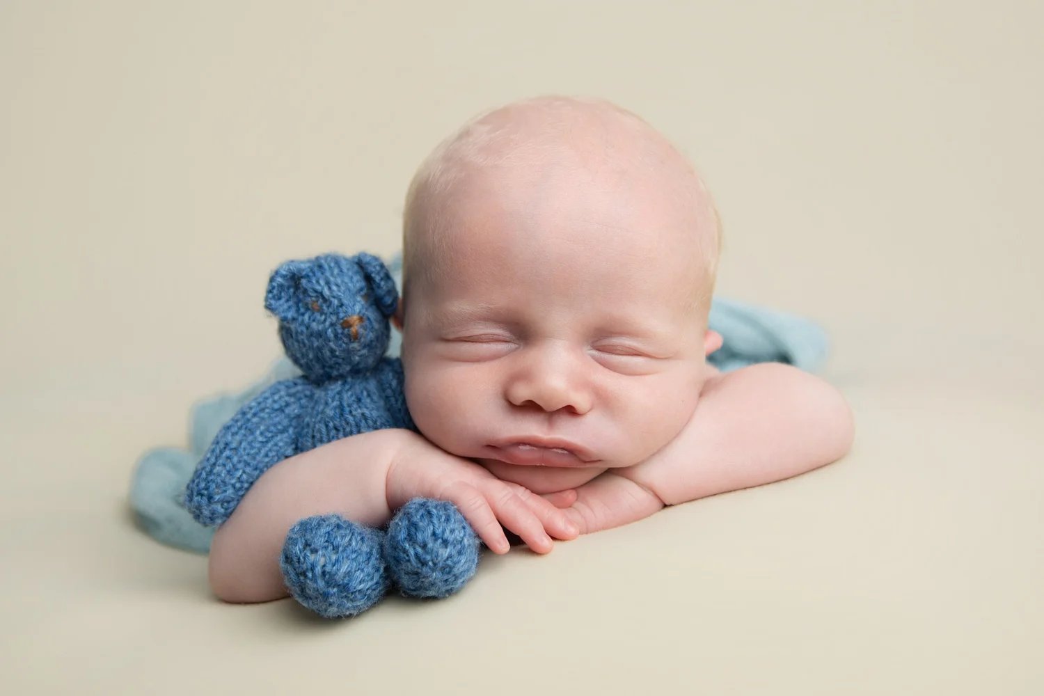 A sleeping newborn baby with a small blue teddy
